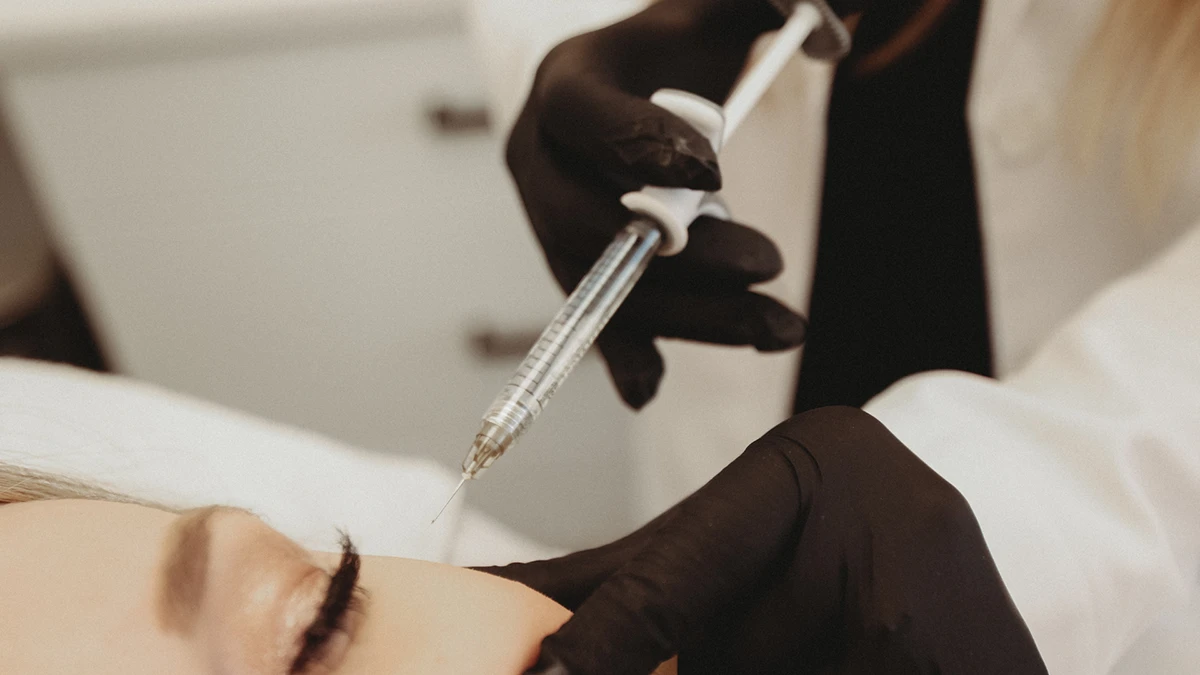 A person in black gloves administers an injection near a patient's eye in a clinical setting. The scene conveys a sense of precision and care. A person in black gloves administers an injection near a patient's eye in a clinical setting. The scene conveys a sense of precision and care.
