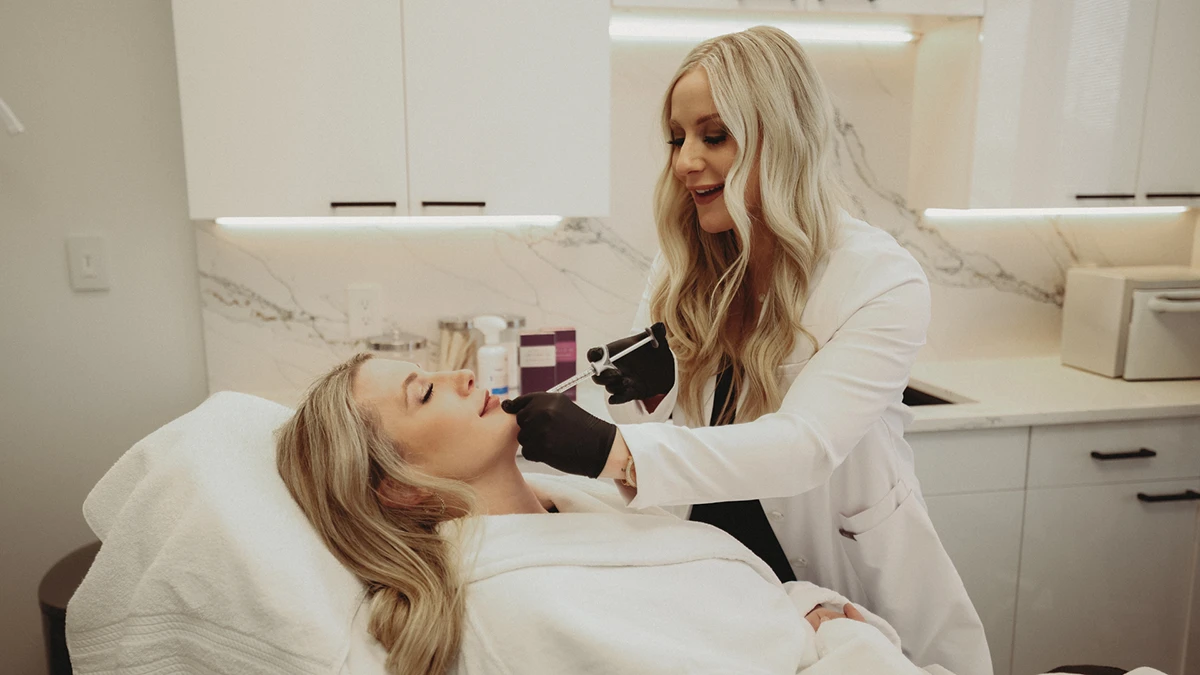 A woman in a white coat and gloves performs a cosmetic procedure on a relaxed woman lying on a treatment bed in a well-lit, modern clinic. A woman in a white coat and gloves performs a cosmetic procedure on a relaxed woman lying on a treatment bed in a well-lit, modern clinic.